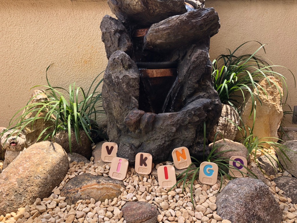 Entre las piedrecitas y plantas de una fuente, están colocadas las letras que forman la palabra VIKINGO